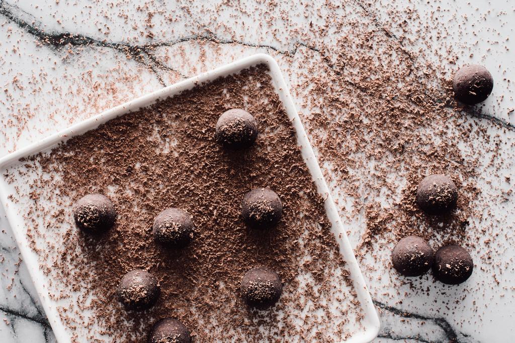 κάτοψη της πλάκας με τρούφες που καλύπτουν από τριμμένη σοκολάτα στο μαρμάρινο τραπέζι  - Φωτογραφία, εικόνα