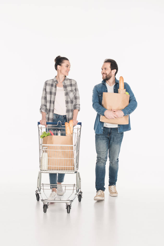 manželka a manžel s papírové balíčky plné potravin a nákupního vozíku při pohledu na sebe izolované na bílém - Fotografie, Obrázek