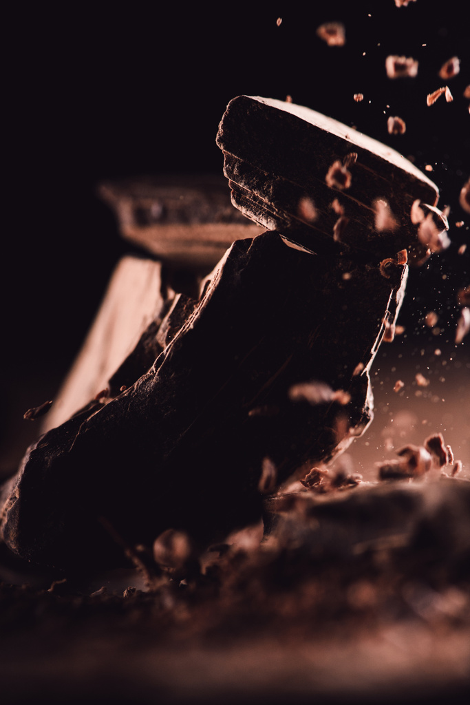  Close-up van geraspte pure chocolade vallen op stukjes chocolade op zwarte achtergrond  - Foto, afbeelding