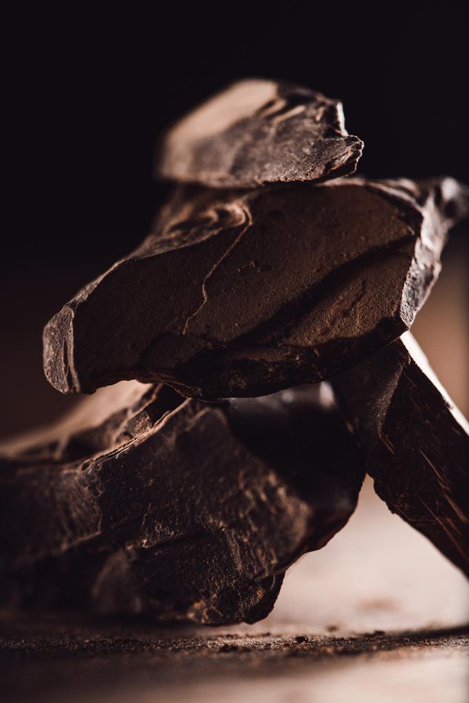 Close-up shot van gearrangeerde stukken van donkere chocolade op houten tafel op zwarte achtergrond  - Foto, afbeelding