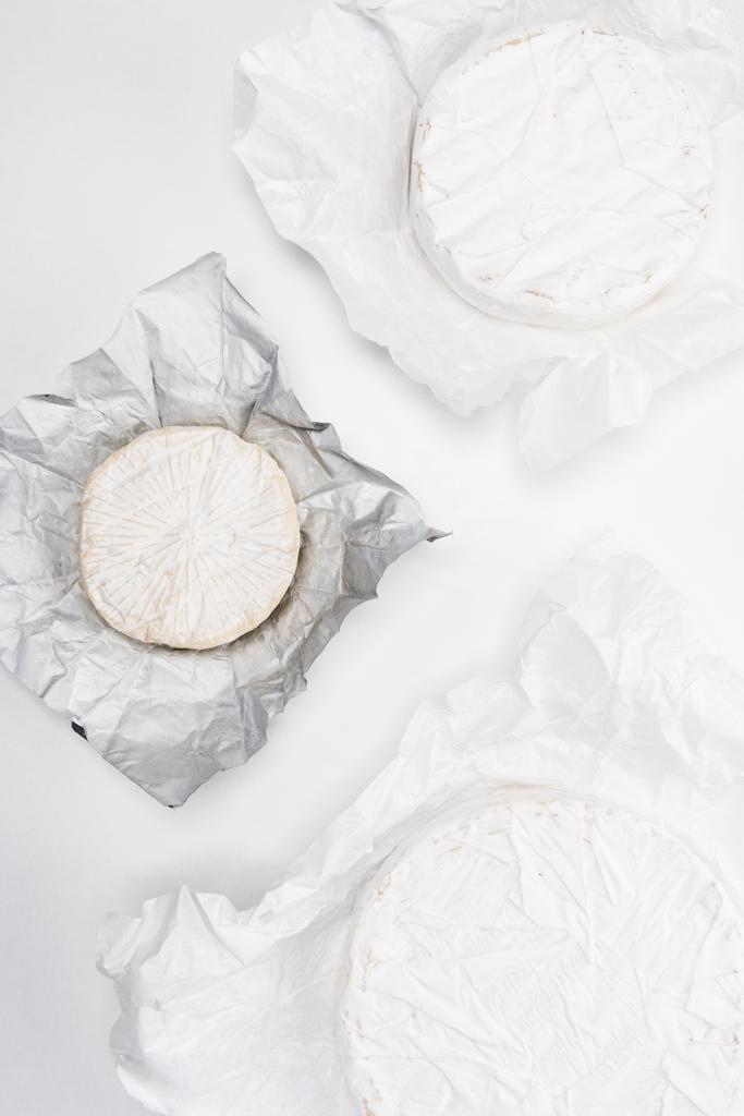 top view of brie cheese heads on crumpled paper and on white tabletop - Photo, Image
