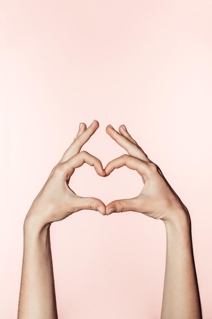Μερική άποψη της γυναίκας που κάνει σύμβολο καρδιά από δάχτυλα που απομονώνονται σε ροζ φόντο  - Φωτογραφία, εικόνα