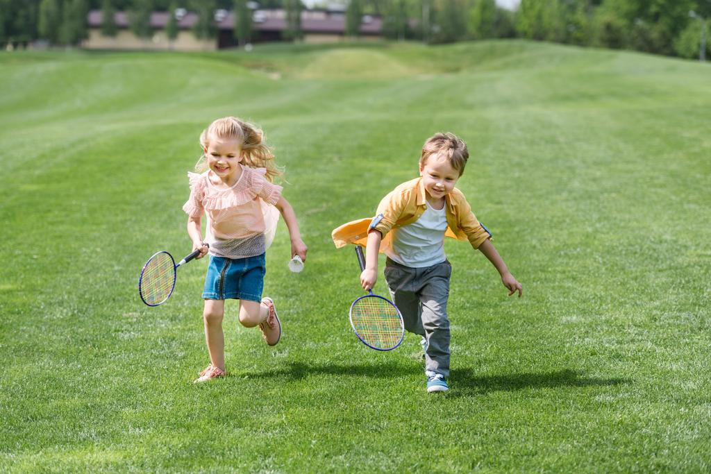 lindos niños sonrientes con raquetas de bádminton corriendo juntos en el parque
  - Foto, imagen