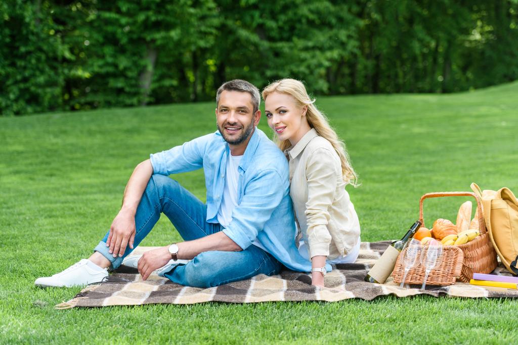 feliz casal sentado em xadrez e sorrindo para a câmera no parque
 - Foto, Imagem