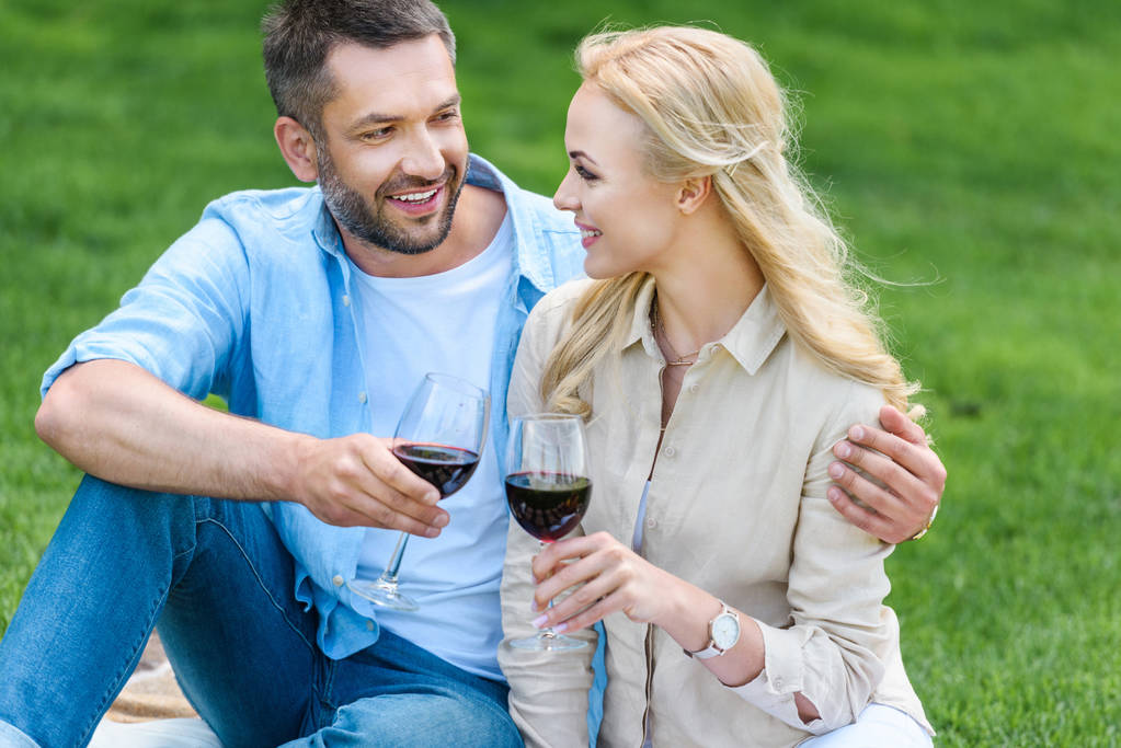 onnellinen nuori pari, jolla on lasit viiniä ja hymyilevät toisiaan piknikillä
 - Valokuva, kuva
