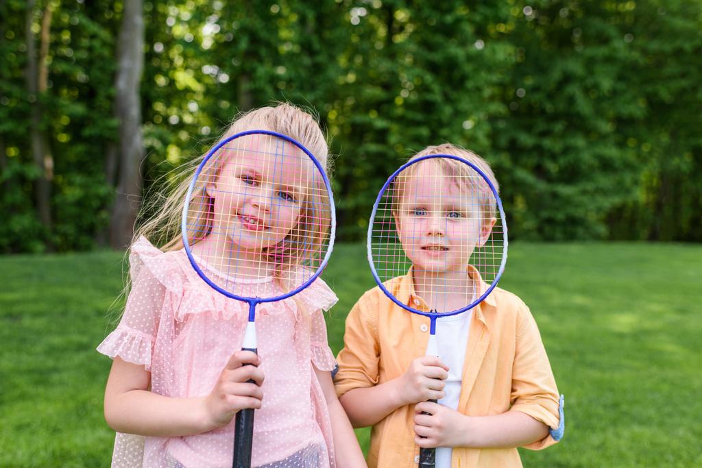 śliczne małe dzieci trzymając badmintonowych i uśmiecha się do kamery w parku - Zdjęcie, obraz