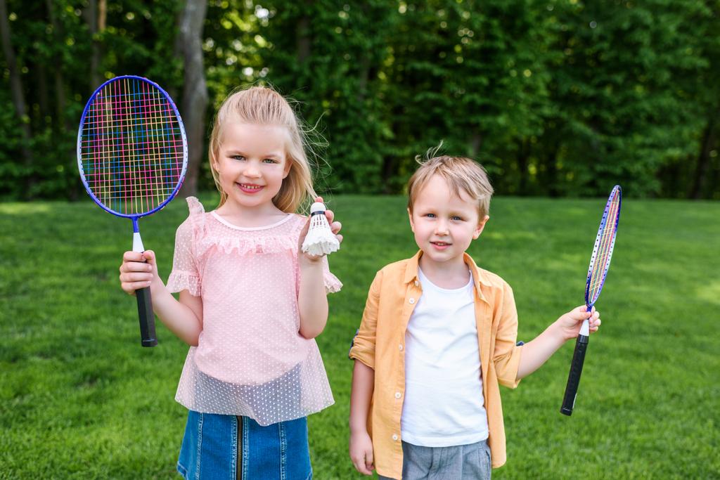 entzückend lächelnde Kinder mit Badmintonschlägern und Federball im Park  - Foto, Bild