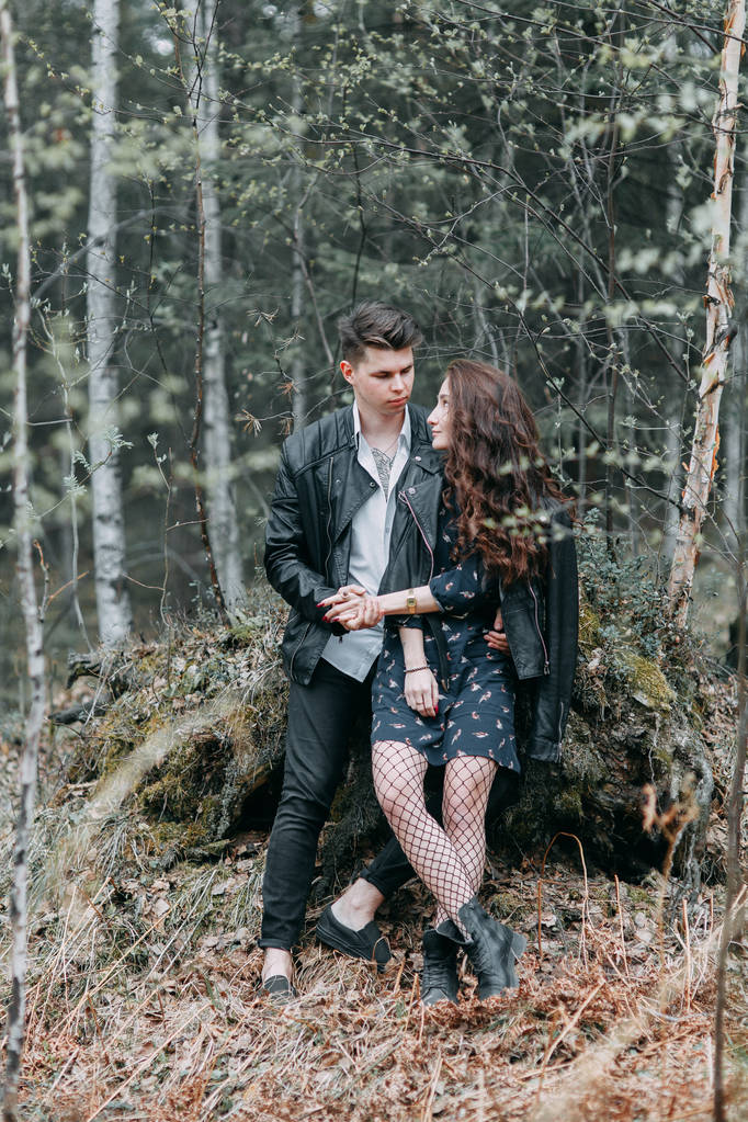 Young stylish couple in the forest, running around the Park and laughing. Modern people on a walk. Beautiful girl with tattoos. Loving young man and girl. mountain Park with pine forest - Photo, Image