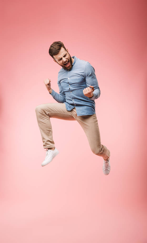 Повна довжина задоволеного молодого чоловіка, який стрибає і святкує успіх ізольовано на рожевому фоні
 - Фото, зображення