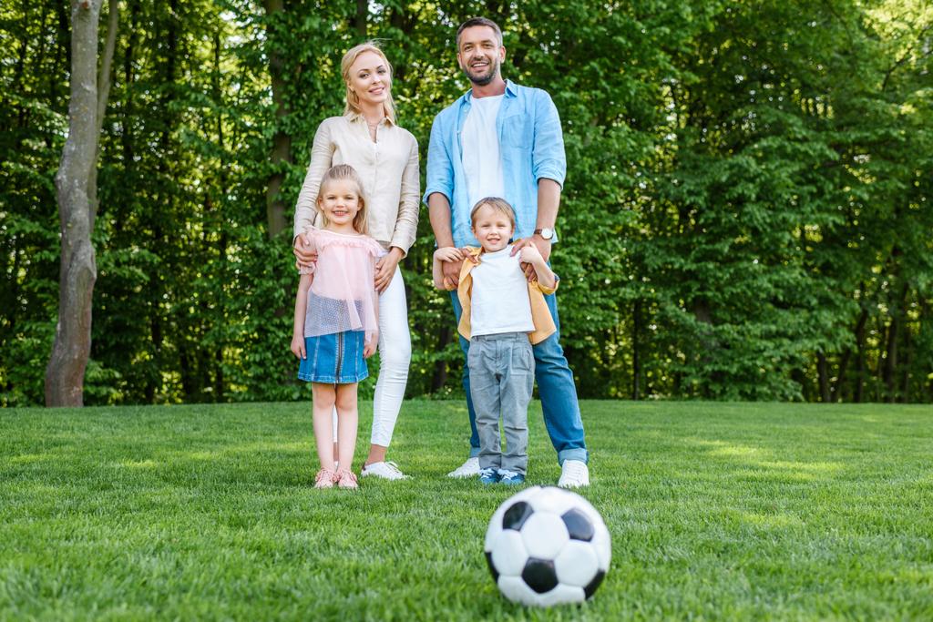 fotbalový míč na trávu a šťastné rodinné stojící v parku - Fotografie, Obrázek
