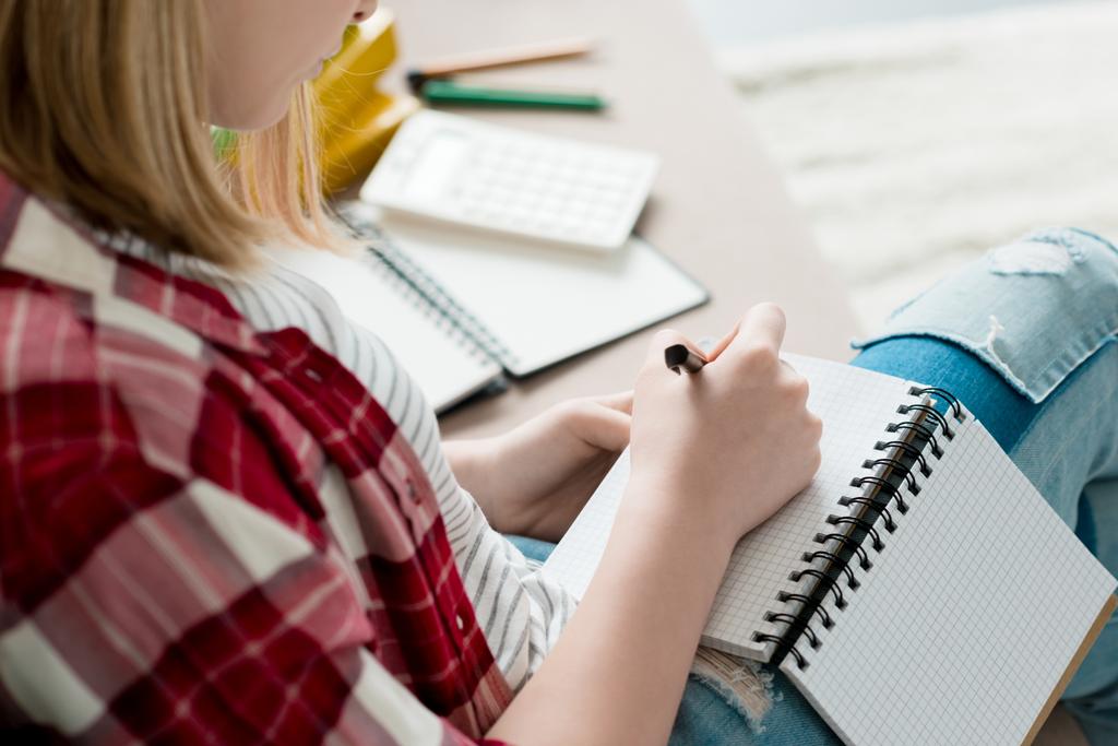 rajattu laukaus teini opiskelija tyttö kirjoittaa muistikirjaan istuessaan sohvalla
 - Valokuva, kuva