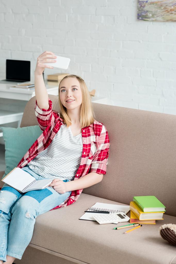 menina estudante adolescente feliz com notebook sentado no sofá e tomando selfie
 - Foto, Imagem