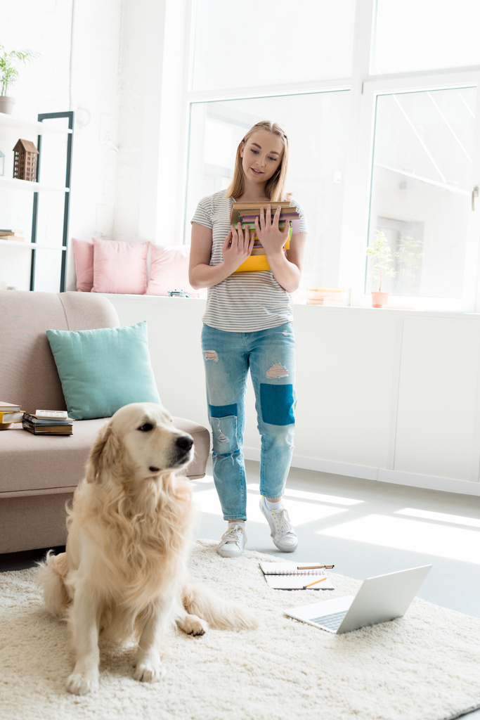 mooie tiener meisje met stapel boeken studeren thuis met haar gouden retriever - Foto, afbeelding