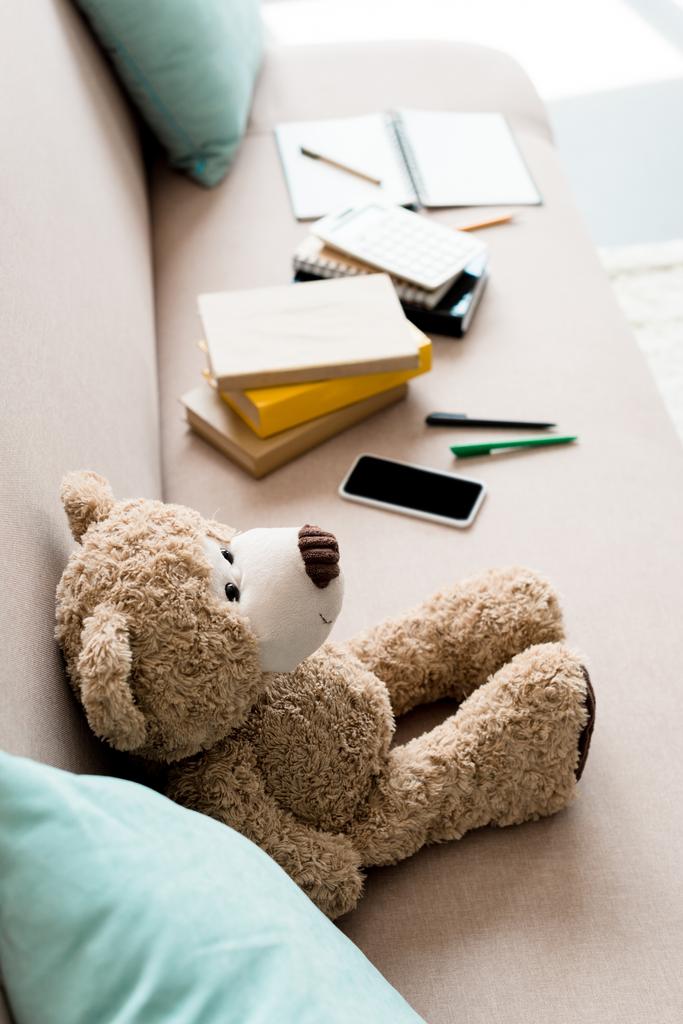 високий кут зору плюшевого ведмедя на дивані зі шкільними приладдям вдома
 - Фото, зображення