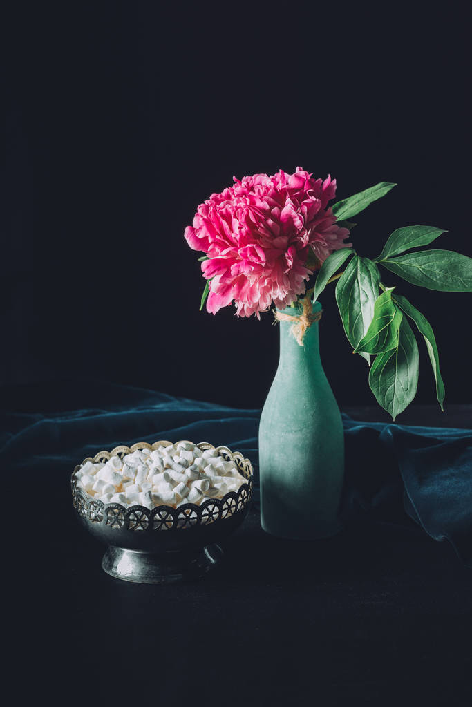peony flower in vase and vintage bowl with sweet marshmallows on dark background - Photo, Image