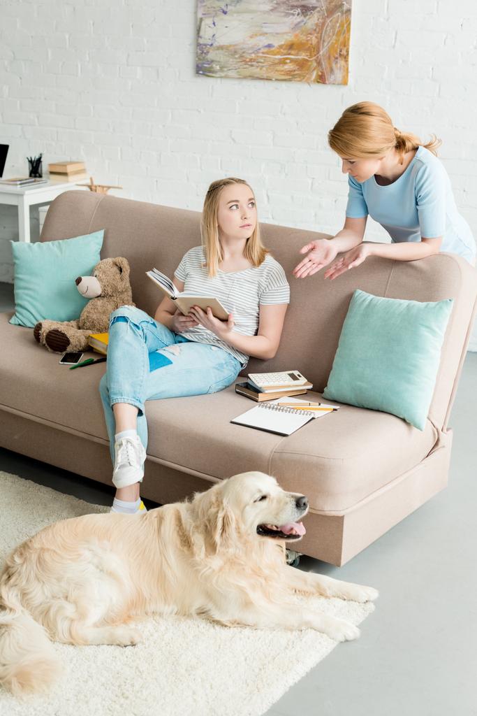mother teaching her daughter at home while she doing homework and their dog lying on floor - Photo, Image