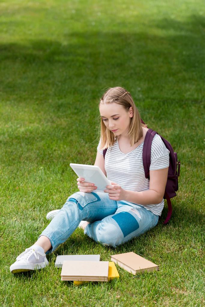 adolescente estudiante chica usando tableta mientras sentado en hierba en jardín
 - Foto, imagen
