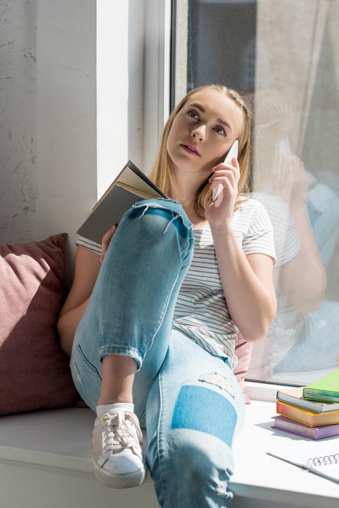 Teenager-Studentin sitzt auf Fensterbank und telefoniert - Foto, Bild
