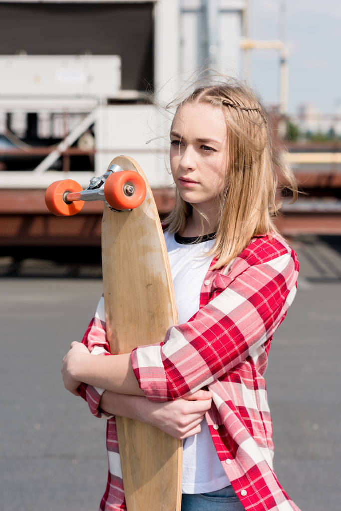 schöne Teenie-Mädchen in rot kariertem Hemd umarmt Skateboard auf dem Dach - Foto, Bild