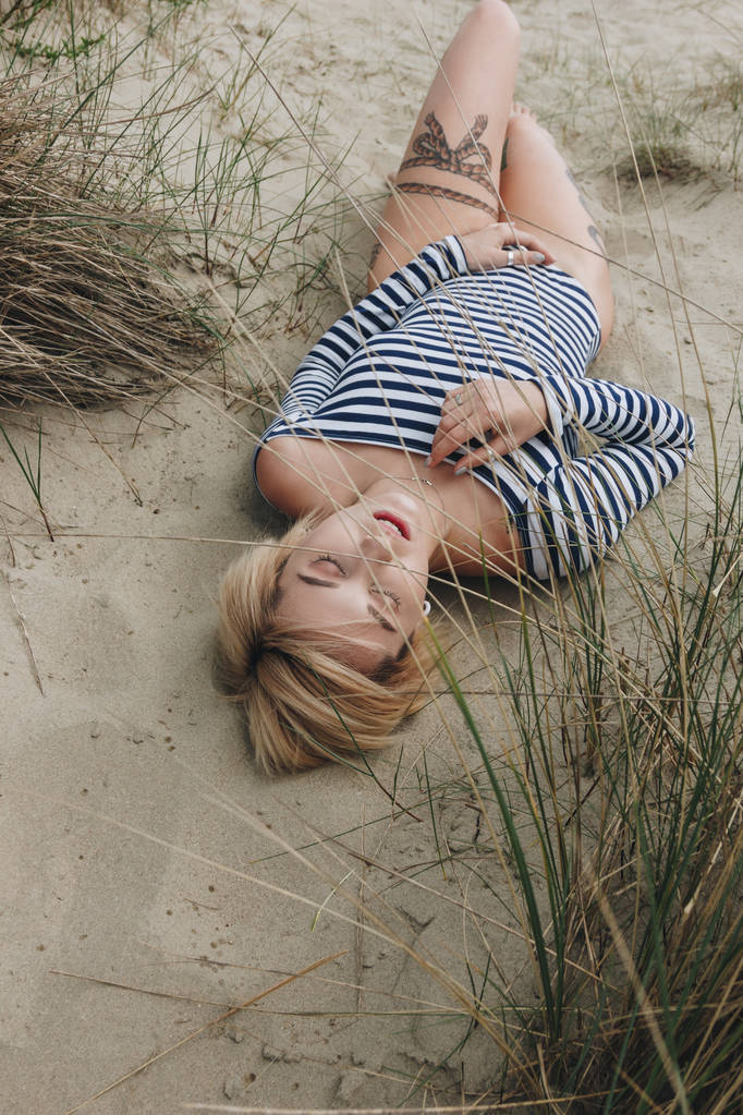 high angle view of sensual young woman in striped bodysuit lying on sand - Photo, Image