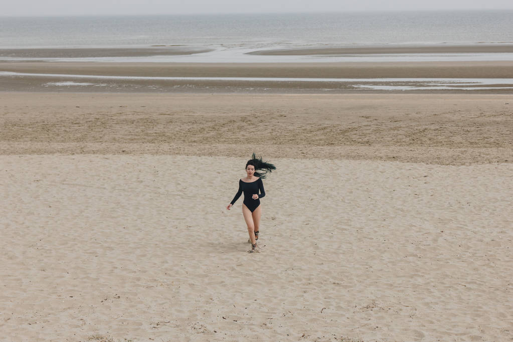 привлекательная молодая женщина в черном купальнике бегает по песчаному побережью
 - Фото, изображение
