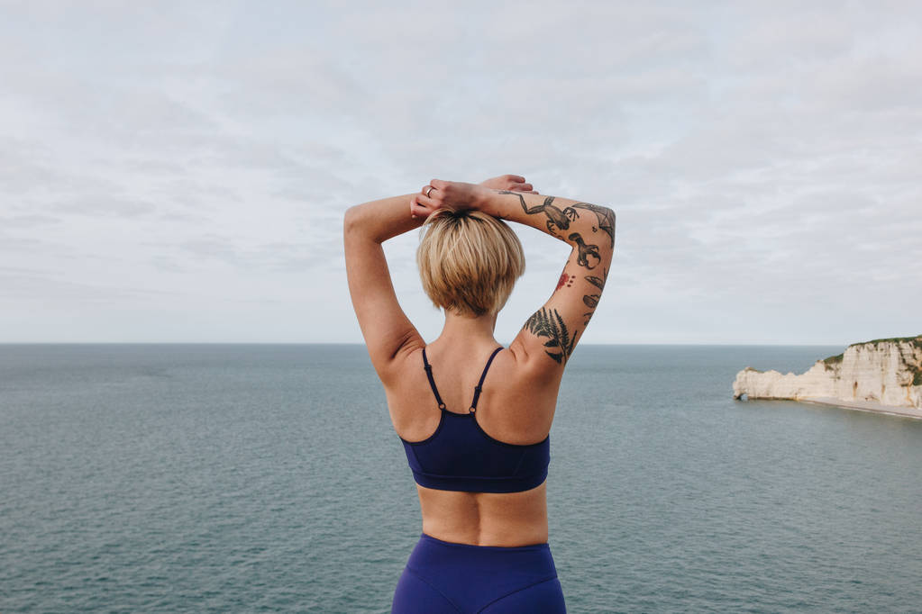 az elegáns sportruházat pózol a tenger közelében, Etretat, Franciaország-tetovált sportos lány hátsó nézet - Fotó, kép
