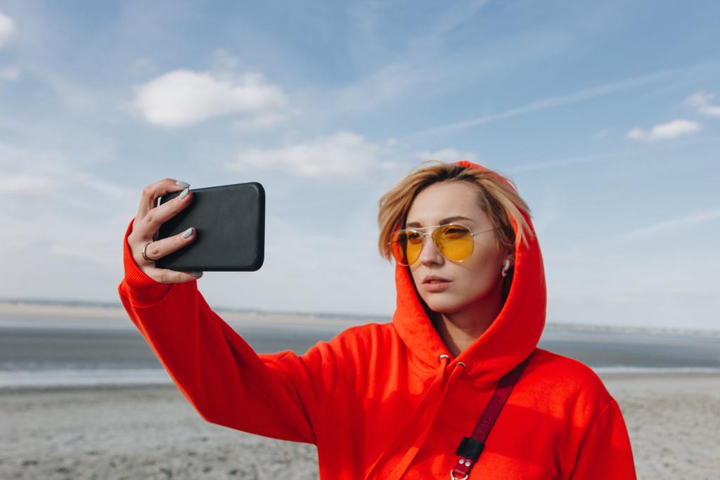 приваблива дівчина в сонцезахисні окуляри, беручи selfie на смартфоні прекрасний пляж, гори Сен Майклс, Франції - Фото, зображення