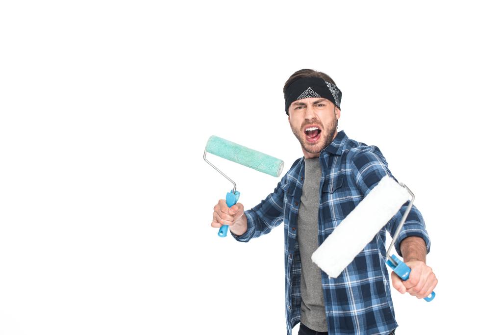 angry young man in headband holding paint rollers isolated on white background  - Photo, Image