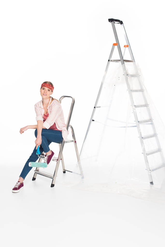Frau in Stirnband sitzt auf kleiner Leiter in der Nähe große Leiter isoliert auf weißem Hintergrund  - Foto, Bild