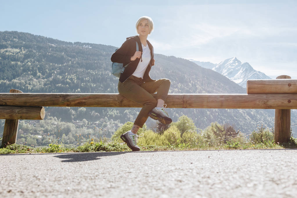 lage hoekmening van meisje met rugzak zittend op een houten hek en kijkt weg in de bergen, mont blanc, Alpen - Foto, afbeelding