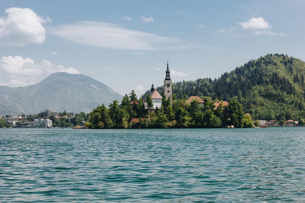 arquitectura antigua y árboles verdes en la orilla en el lago de montaña escénico, sangró, slovenia
 - Foto, Imagen