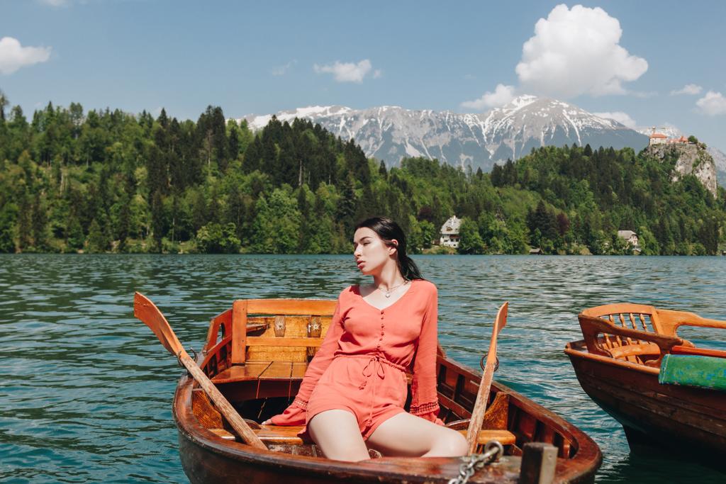 bela jovem mulher sentada em barco no lago de montanha tranquilo cênico, sangrado, slovenia
 - Foto, Imagem