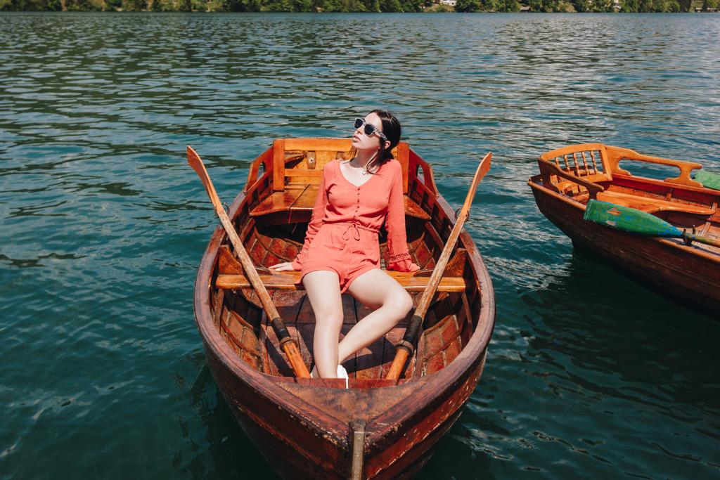 bella ragazza in occhiali da sole seduto su una barca di legno sul lago
 - Foto, immagini