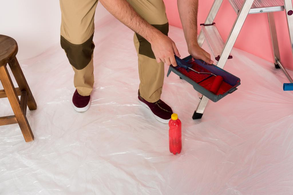 Zugeschnittenes Bild eines Mannes bei der Arbeit, der Farbwalze in Rollbrett taucht - Foto, Bild