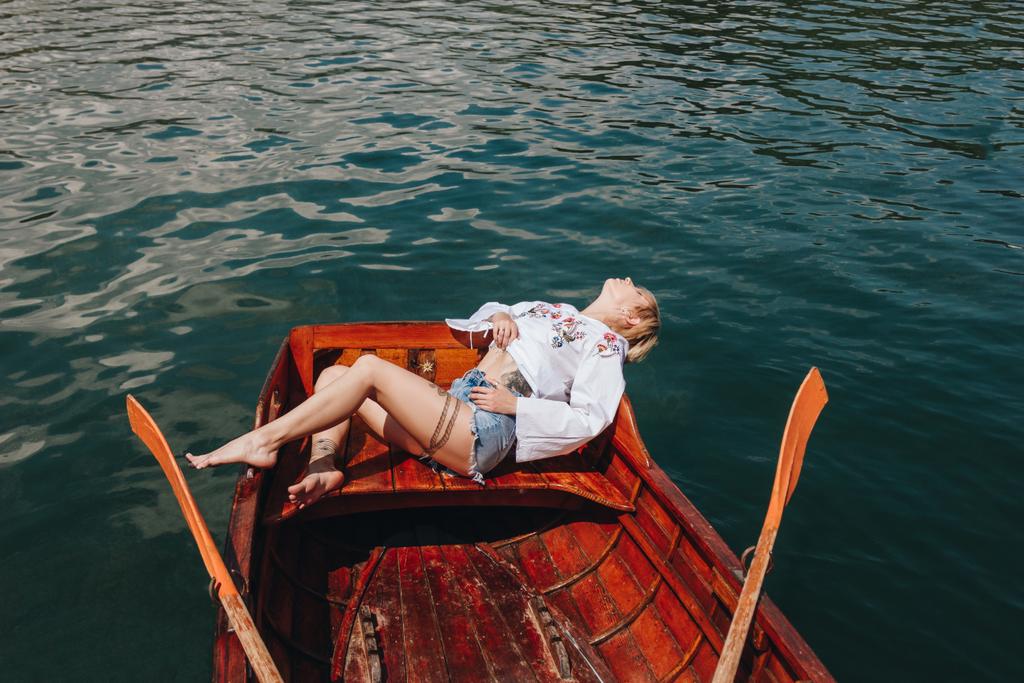 високий кут зору молода жінка розслабляється в дерев'яному човні на озері
 - Фото, зображення