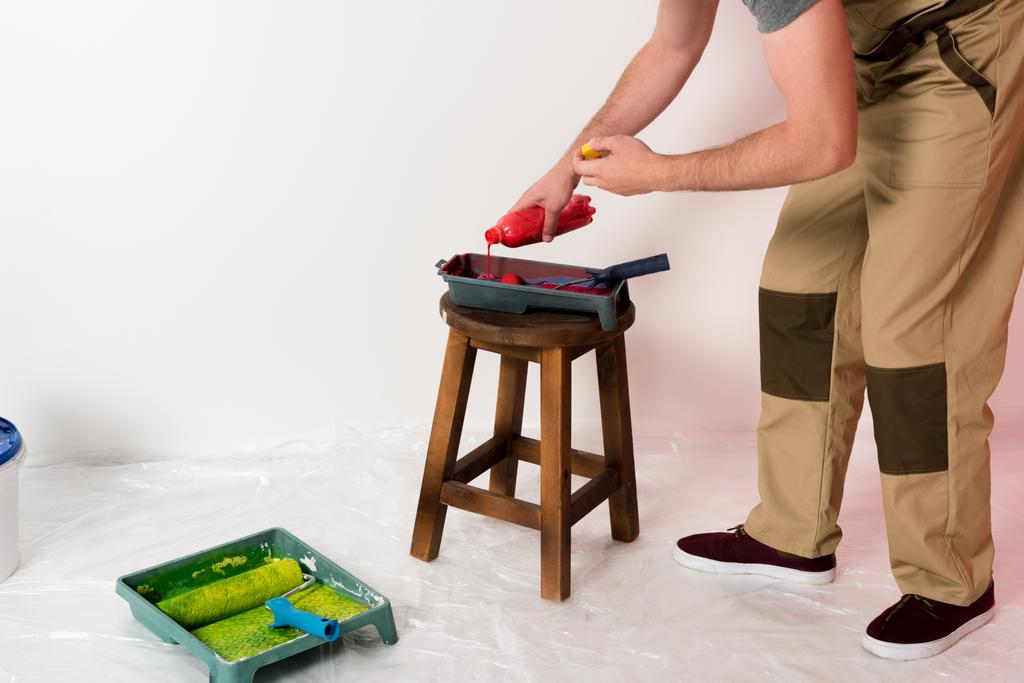 abgeschnittener Schuss von Mann im Arbeitsanzug, der Farbe aus Flasche in Rollcontainer auf Stuhl gießt  - Foto, Bild