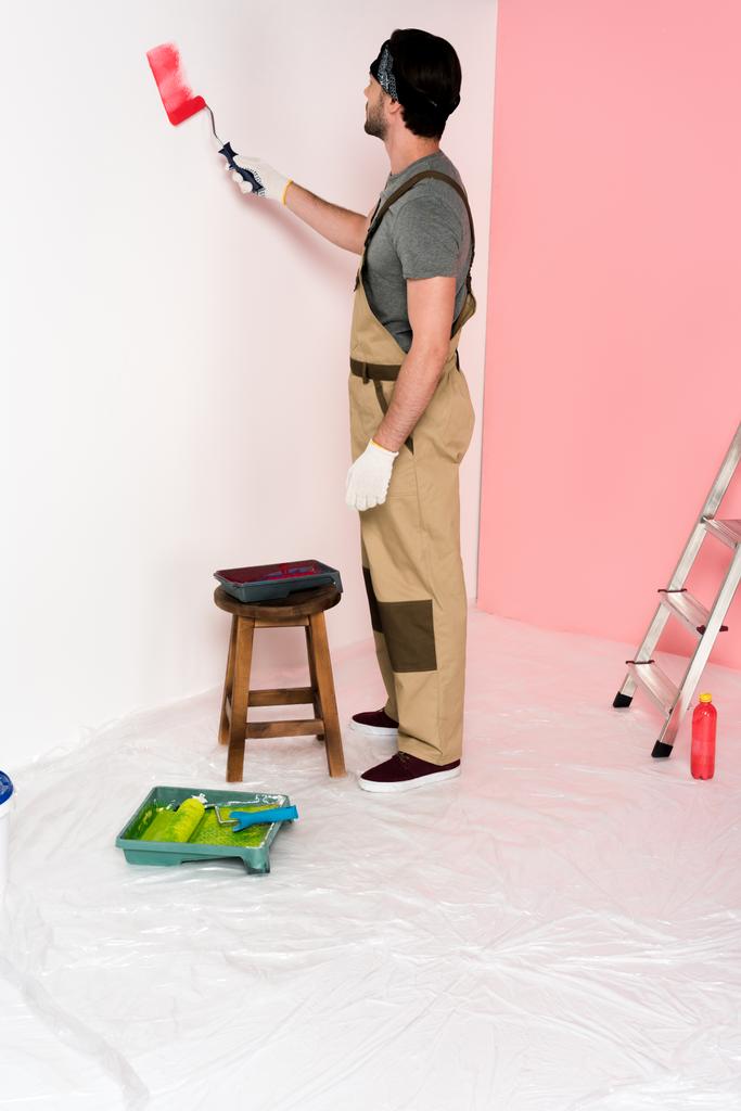 Молодой человек в работе в целом и повязка стены в красном цвете с помощью краски ролика возле стула с подносом
 - Фото, изображение