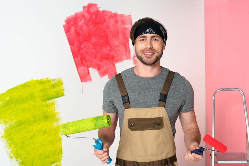 fiatal mosolygó ember, a munka teljes előtt festett fal festék görgőkkel  - Fotó, kép