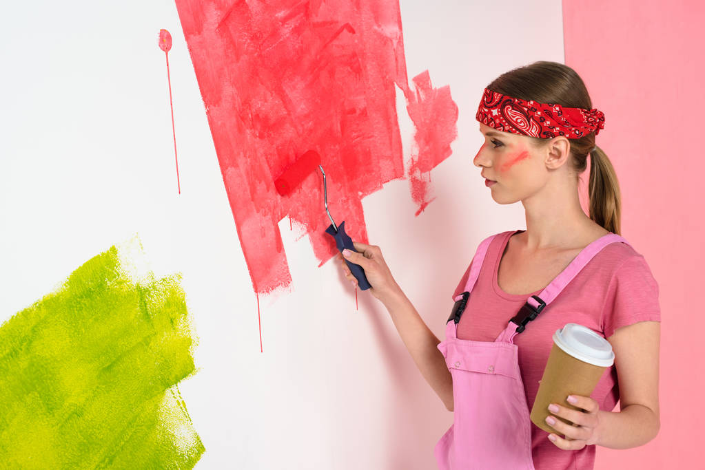 mujer joven con taza de café pintura pared en rojo por rodillo de pintura
  - Foto, Imagen