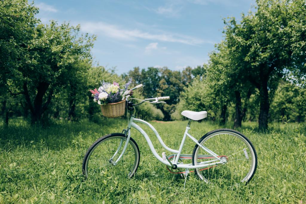 επιλεκτική εστίαση του ρετρό ποδήλατο με ψάθινο καλάθι γεμάτο λουλούδια στο ύπαιθρο - Φωτογραφία, εικόνα