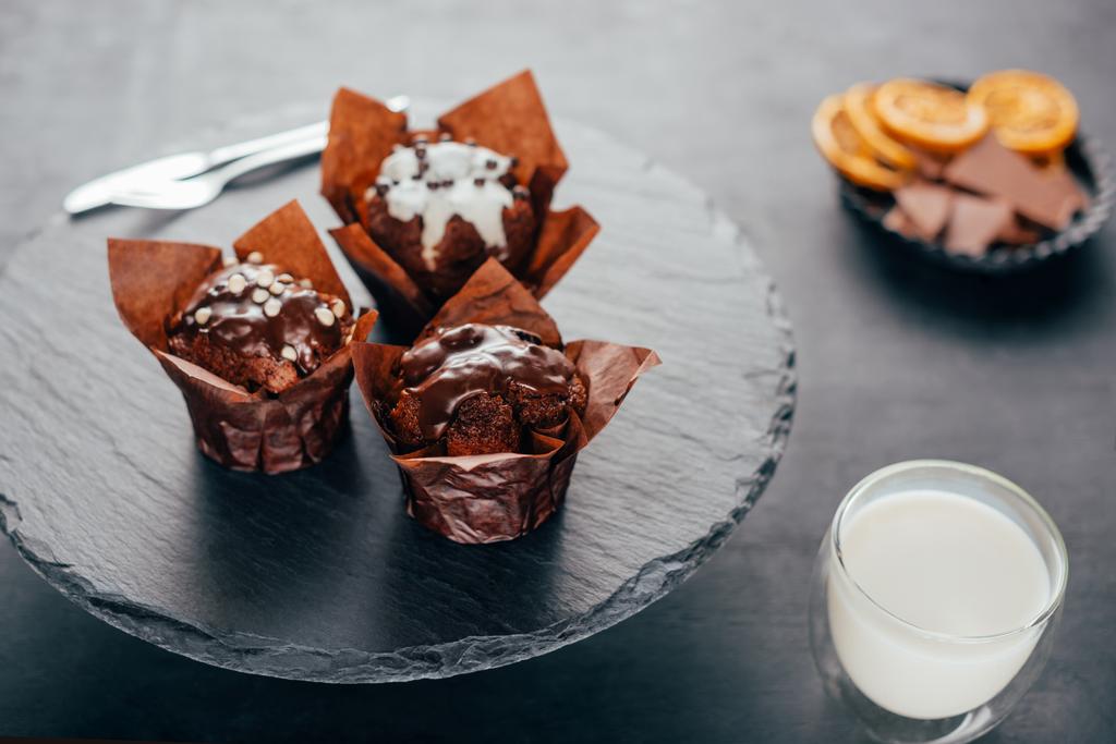 Zoete cupcakes met chocolade chips en glazen melk op leisteen bord - Foto, afbeelding