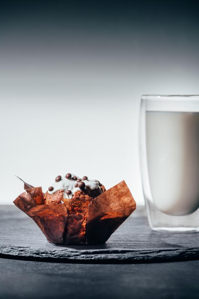 Сладкий кекс с шоколадной крошкой и стаканом молока на доске
 - Фото, изображение