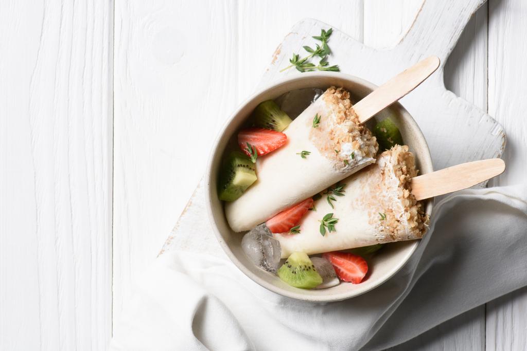 Heerlijke ijslollys met aardbei en kiwi in kom - Foto, afbeelding
