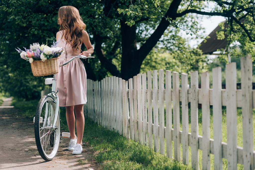 nuori nainen mekko retro polkupyörän kanssa paju kori täynnä kukkia maaseudulla
 - Valokuva, kuva
