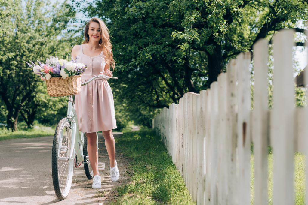 田舎で花の完全な枝編み細工品バスケット レトロな自転車とドレスの若い美しい女性 - 写真・画像