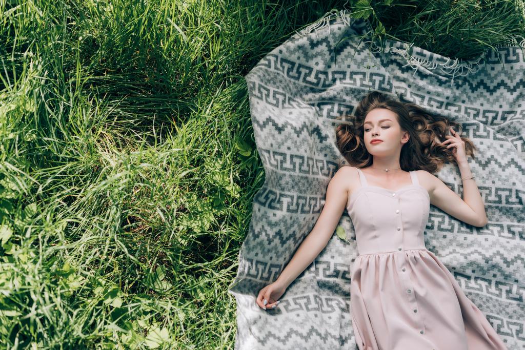 overhead view of beautiful thoughtful woman in dress lying on blank on green grass in park - Photo, Image