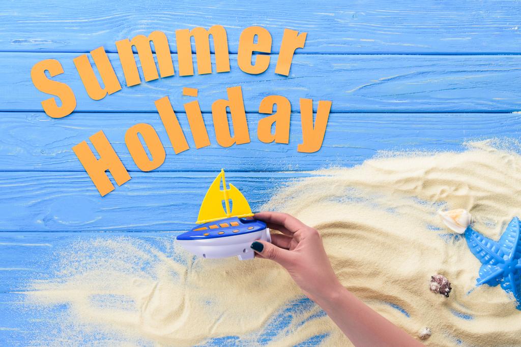 Manos femeninas con barco de juguete por inscripción de vacaciones de verano sobre fondo de madera azul
 - Foto, Imagen