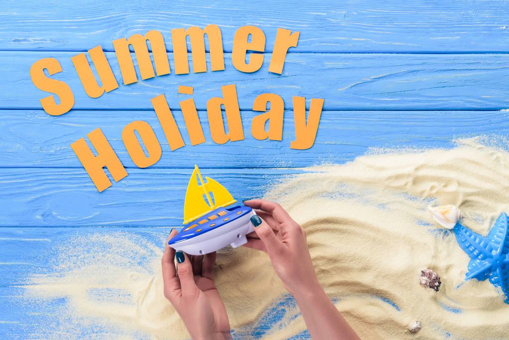 Mani femminili con barca giocattolo per iscrizione vacanze estive su sfondo blu in legno
 - Foto, immagini