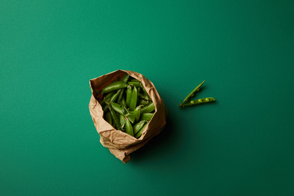 緑色の表面にえんどう豆が入った紙袋の上から見る - 写真・画像