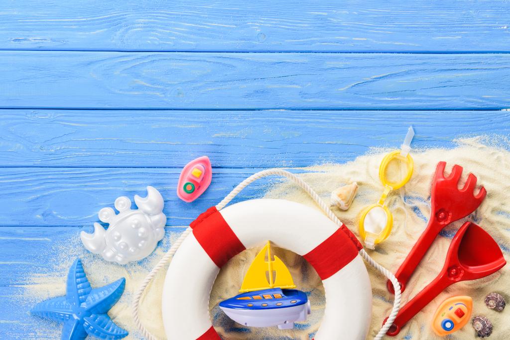 Anel de vida e brinquedos de praia em fundo de madeira azul
 - Foto, Imagem